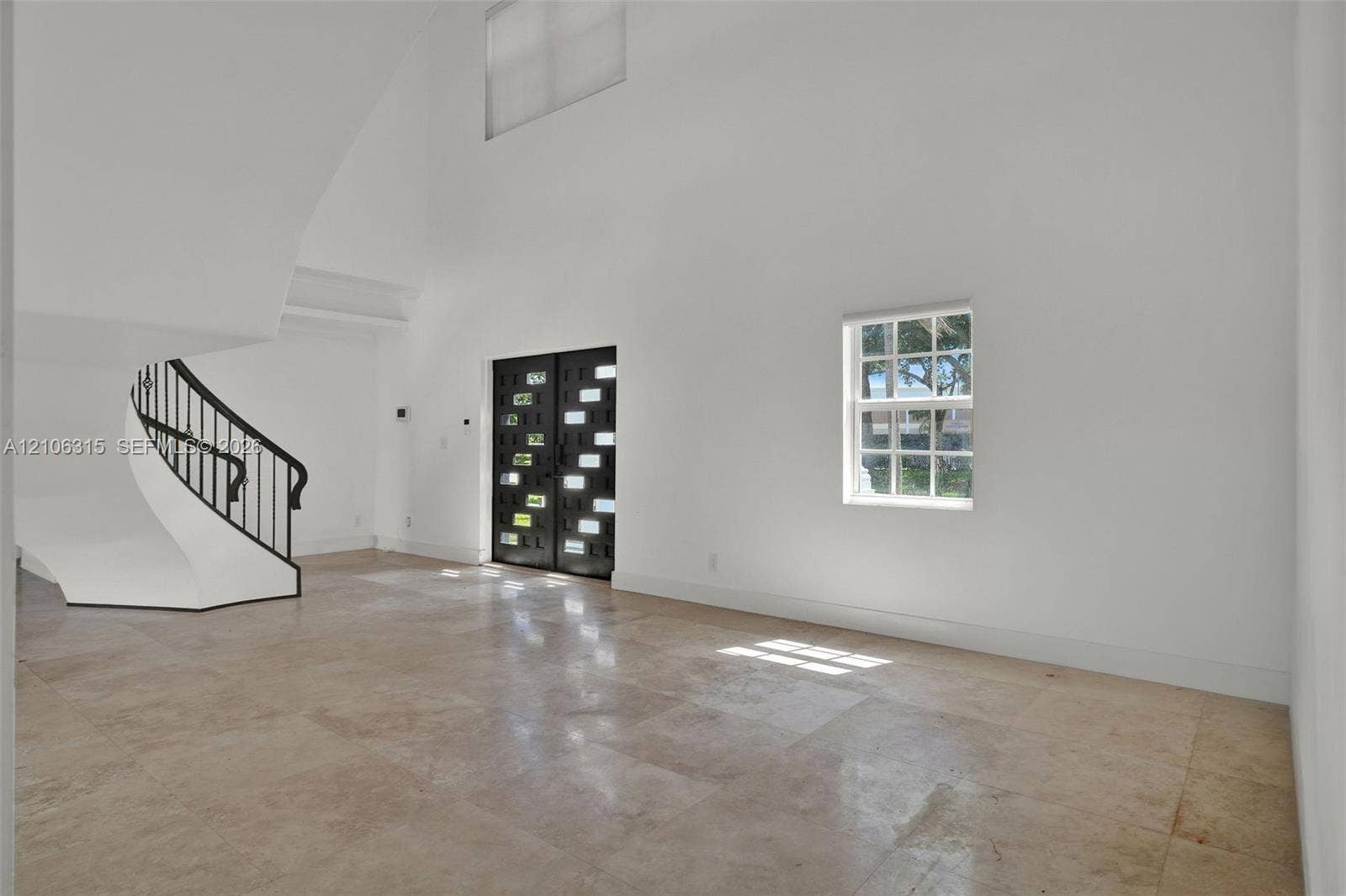 2319 NE 35th Drive, Fort Lauderdale, FL 33308 Double-height entry foyer featuring large-format natural stone flooring, a sculptural curved staircase with a black metal railing, and an architectural double-door entryway with integrated light inserts