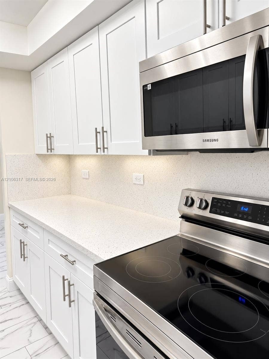 Kitchen featuring white shaker-style cabinetry, stainless steel appliances, speckled stone-finish countertops, and white stone-finish backsplash