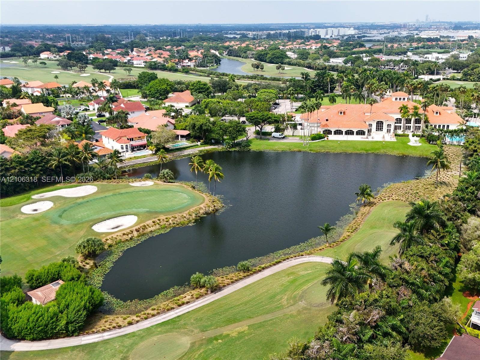 9921 NW 51st Lane, Doral, FL 33178 Aerial perspective showcasing a large-scale residence with a tile roof situated on a golf course featuring a water hazard, sand bunkers, and mature landscaping