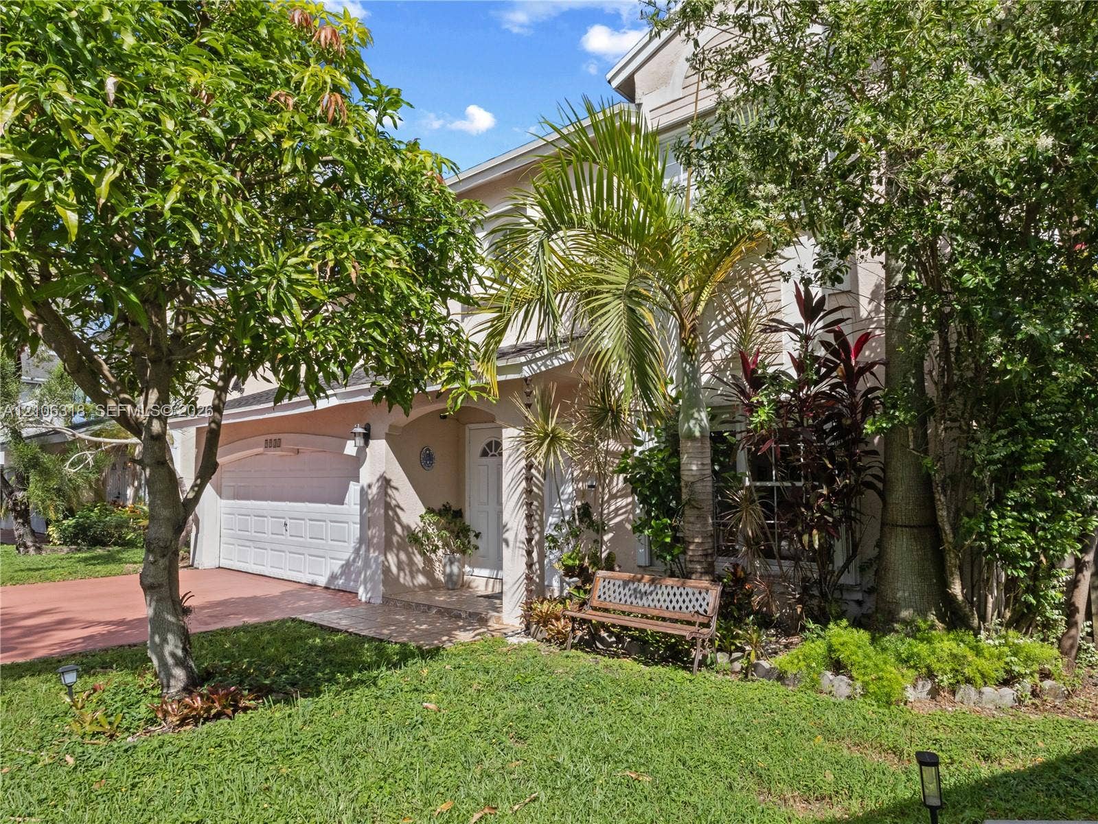 9921 NW 51st Lane, Doral, FL 33178 Two-story exterior featuring a stucco facade, an attached two-car garage with a sectional door, a covered entryway, and mature tropical landscaping