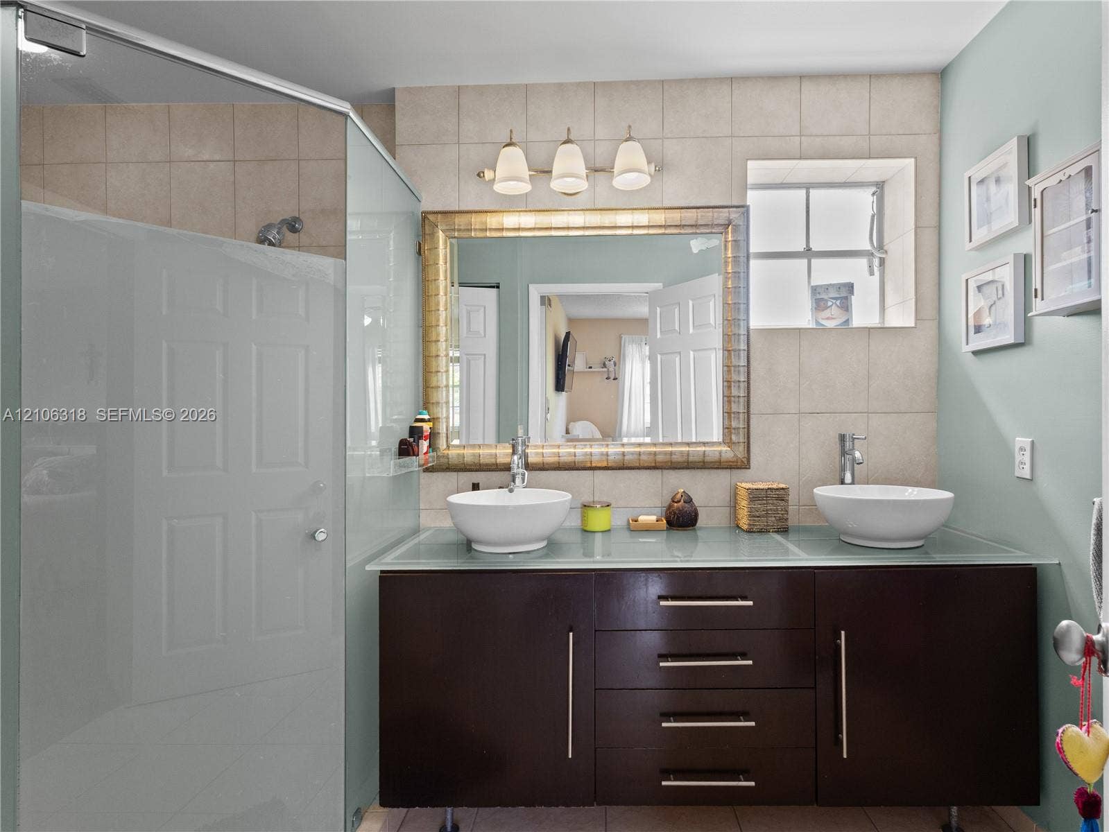 9921 NW 51st Lane, Doral, FL 33178 Floating vanity with a frosted glass countertop, dual white vessel sinks, polished chrome fixtures, and a framed wall mirror