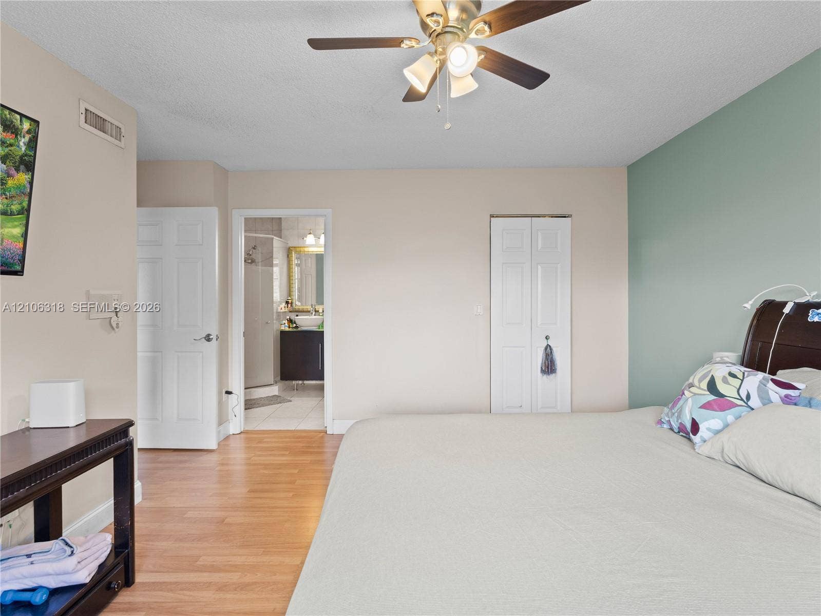 9921 NW 51st Lane, Doral, FL 33178 Bedroom featuring wood-finish flooring, a ceiling fan with integrated lighting, a dual-panel closet door, and an accent wall