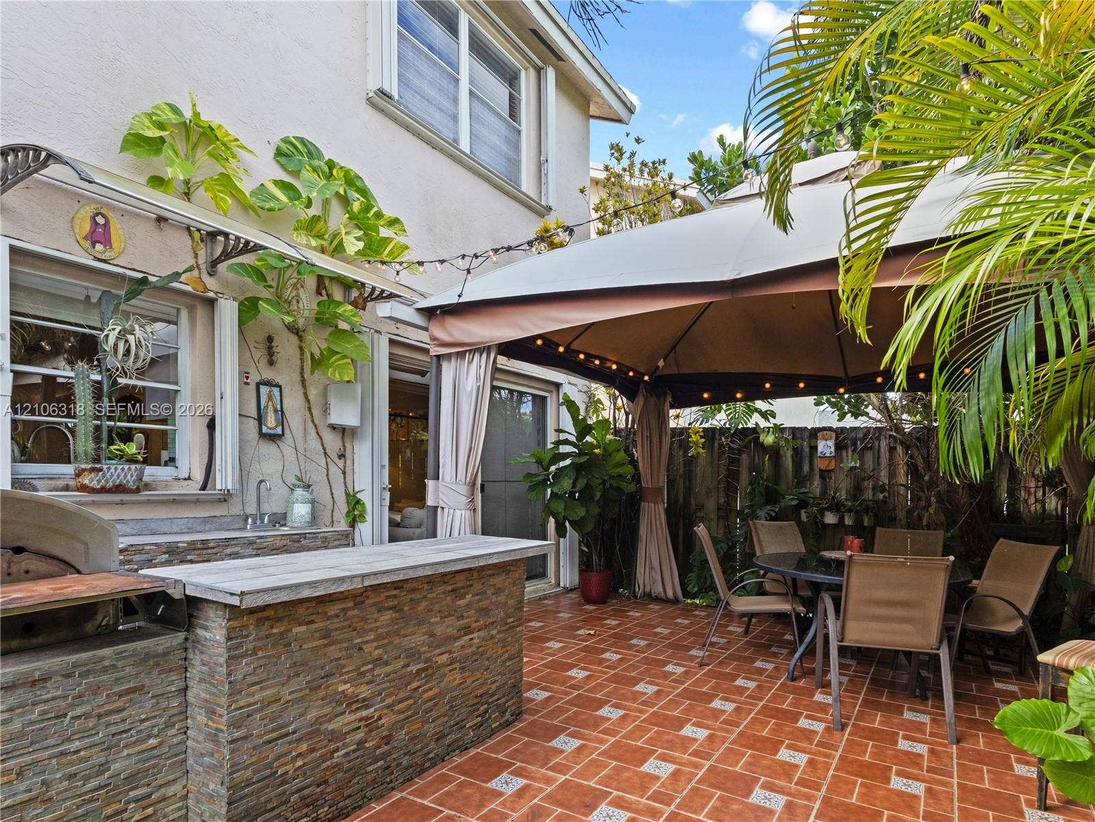 9921 NW 51st Lane, Doral, FL 33178 Outdoor kitchen featuring a stacked-stone facade, built-in prep counter, sink, and grill area on a ceramic tiled patio