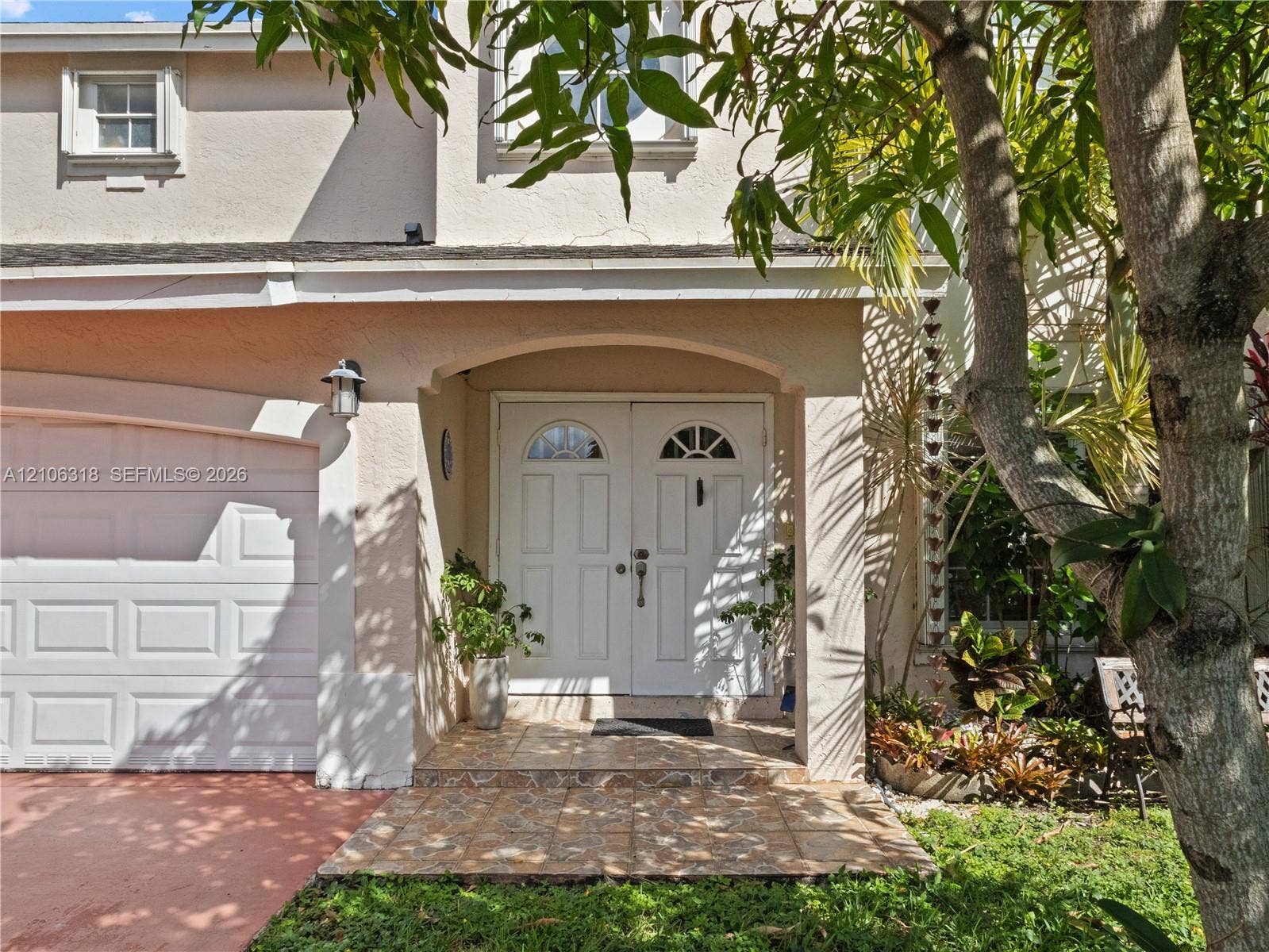 9921 NW 51st Lane, Doral, FL 33178 Stucco exterior with a covered entryway, arched portico, double-door entry featuring semi-circular glass inserts, and an attached single-car garage