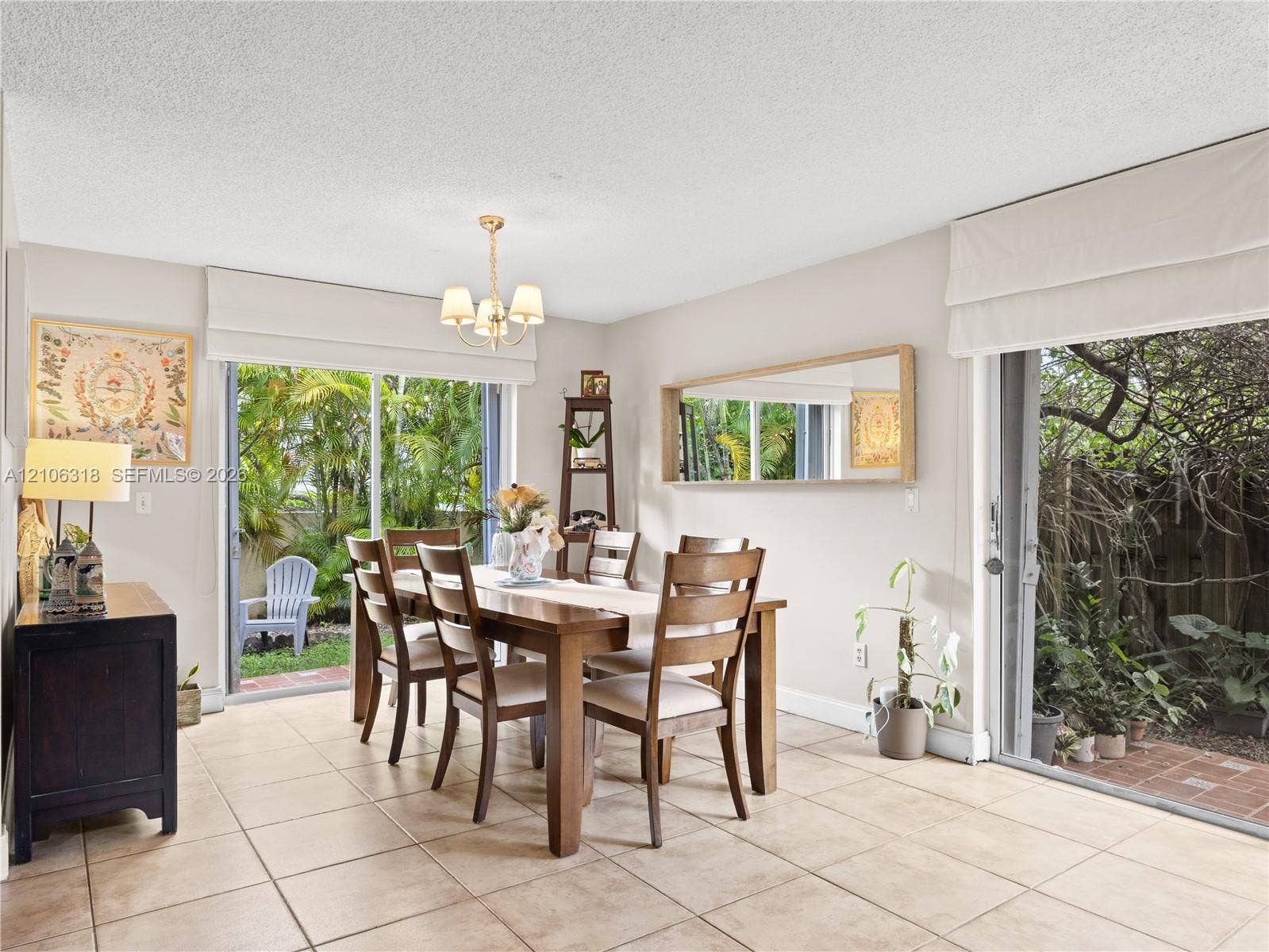 9921 NW 51st Lane, Doral, FL 33178 Dining space featuring large-format tile flooring, dual sliding glass doors, a decorative chandelier, and a wall-mounted rectangular mirror