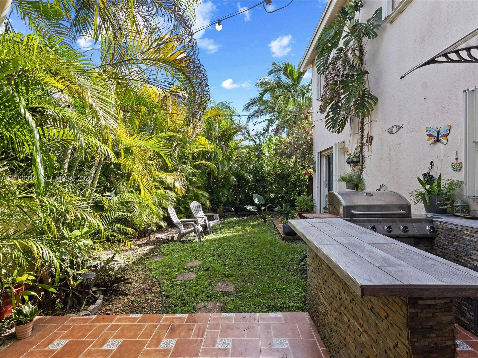 9921 NW 51st Lane, Doral, FL 33178 Outdoor patio featuring tile flooring, built-in stone-clad grill station with stone countertop, and mature palm landscaping