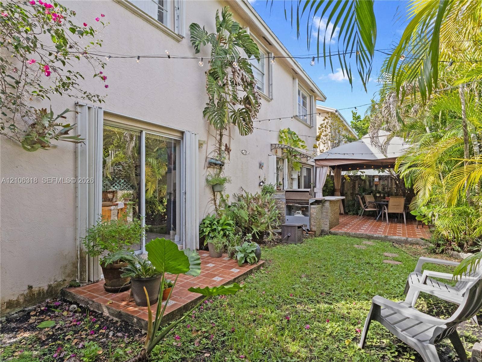 9921 NW 51st Lane, Doral, FL 33178 Private backyard featuring a paved tile patio, built-in outdoor kitchen with stone veneer, and lush greenery