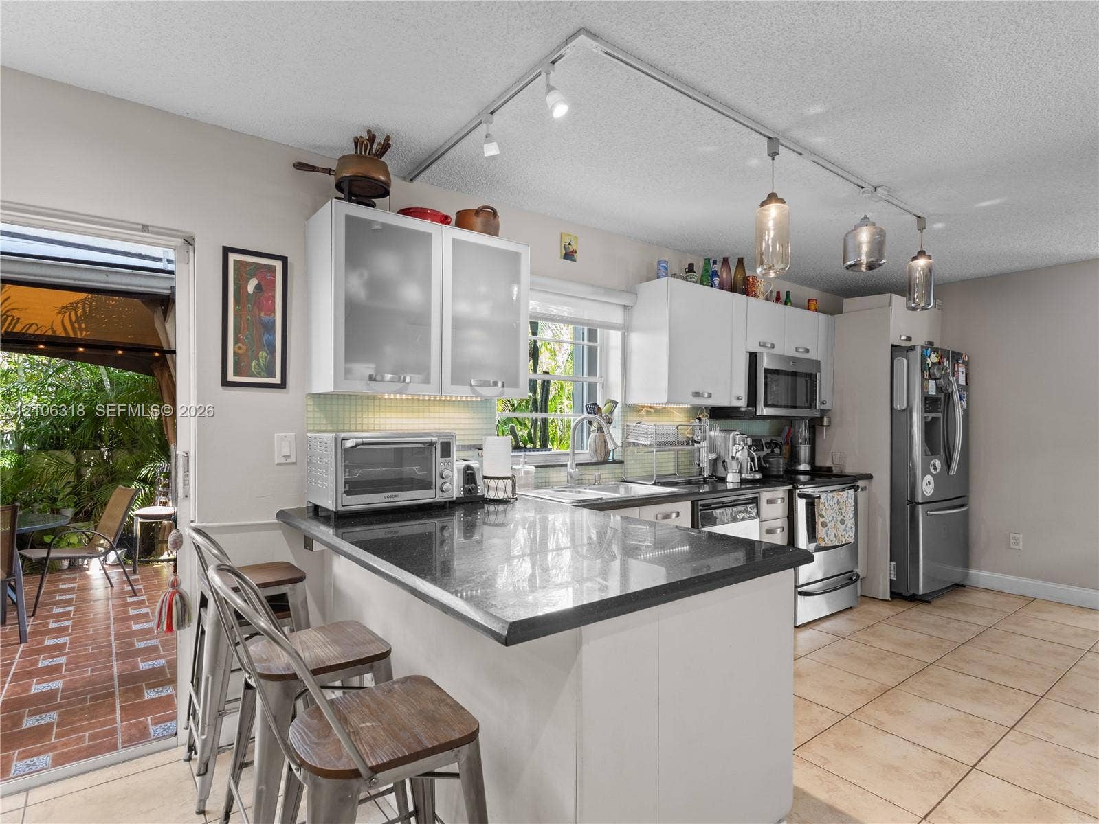 9921 NW 51st Lane, Doral, FL 33178 Kitchen featuring white cabinetry with glass-panel upper doors, dark stone-finish countertops, stainless steel appliances, and adjustable track lighting