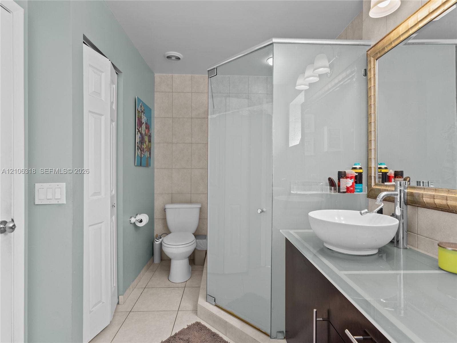 9921 NW 51st Lane, Doral, FL 33178 Vanity featuring a glass countertop and oval vessel sink, framed wall mirror, corner glass-enclosed shower, and tile flooring