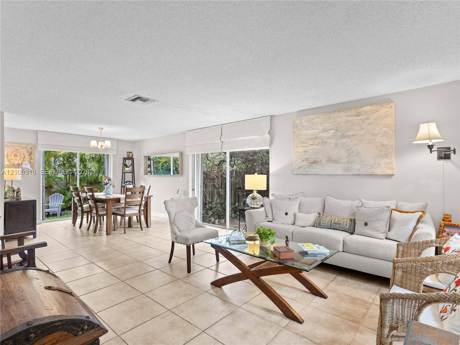 9921 NW 51st Lane, Doral, FL 33178 Open-concept living space featuring neutral ceramic tile flooring, dual sliding glass doors, and wall-mounted light fixtures
