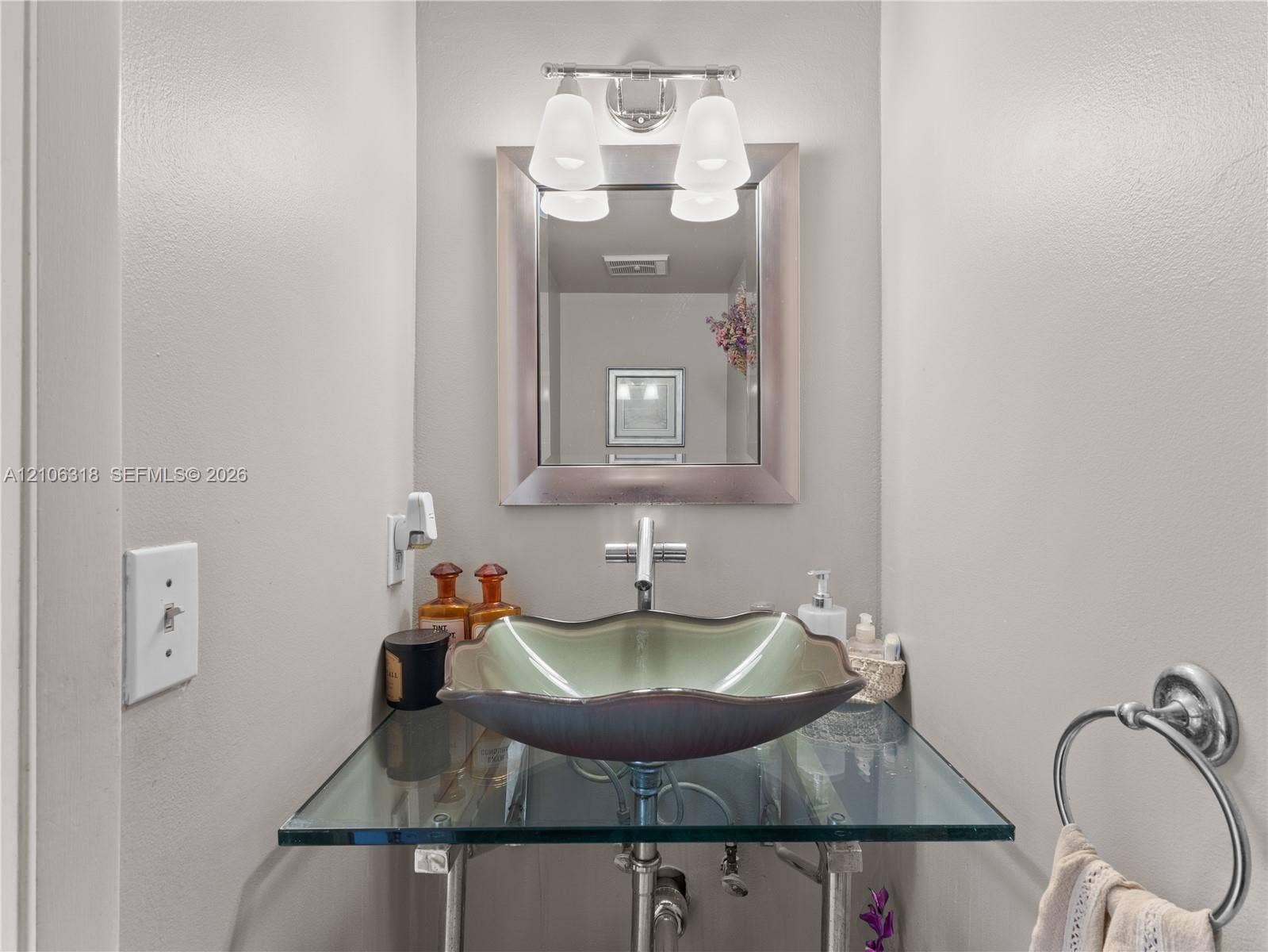 9921 NW 51st Lane, Doral, FL 33178 Floating glass vanity with a scalloped basin, chrome single-handle faucet, wall-mounted mirror with a metallic frame, and a dual-light fixture