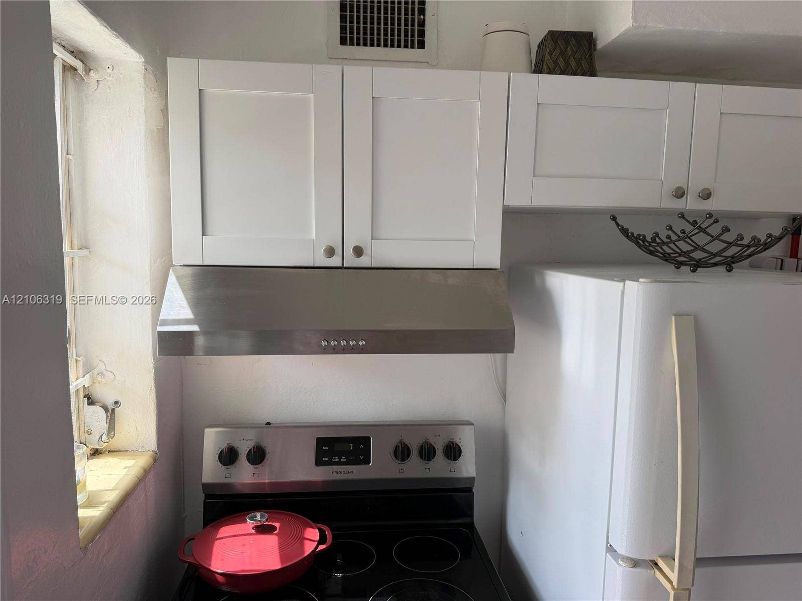 Shaker-style white cabinetry, stainless steel range hood, and electric range with stainless steel control panel