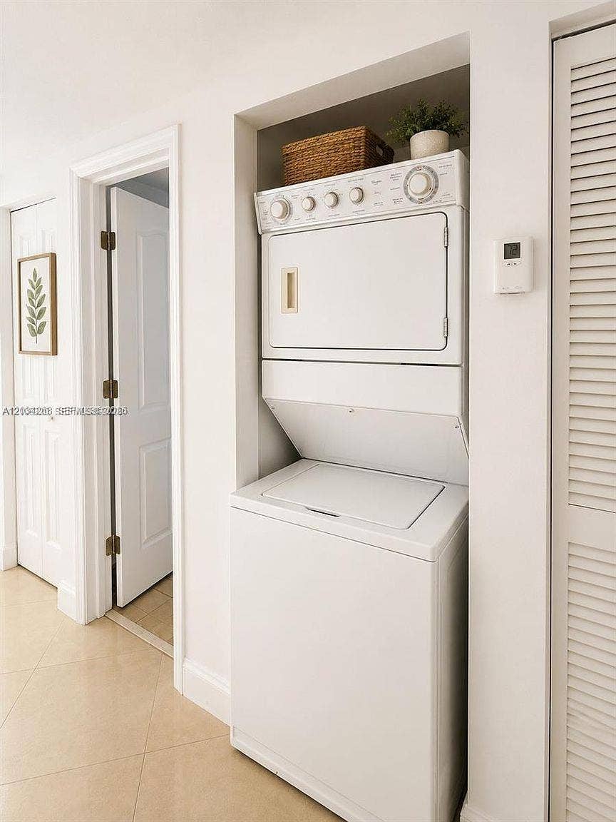 Built-in laundry alcove featuring a stacked washer and dryer unit, tiled flooring, and louvered closet doors