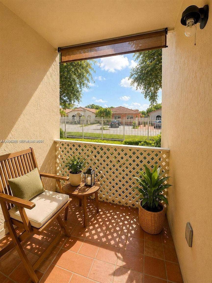 Covered terrace featuring terra-cotta tile flooring, white diamond-pattern lattice railing, and a retractable sun shade