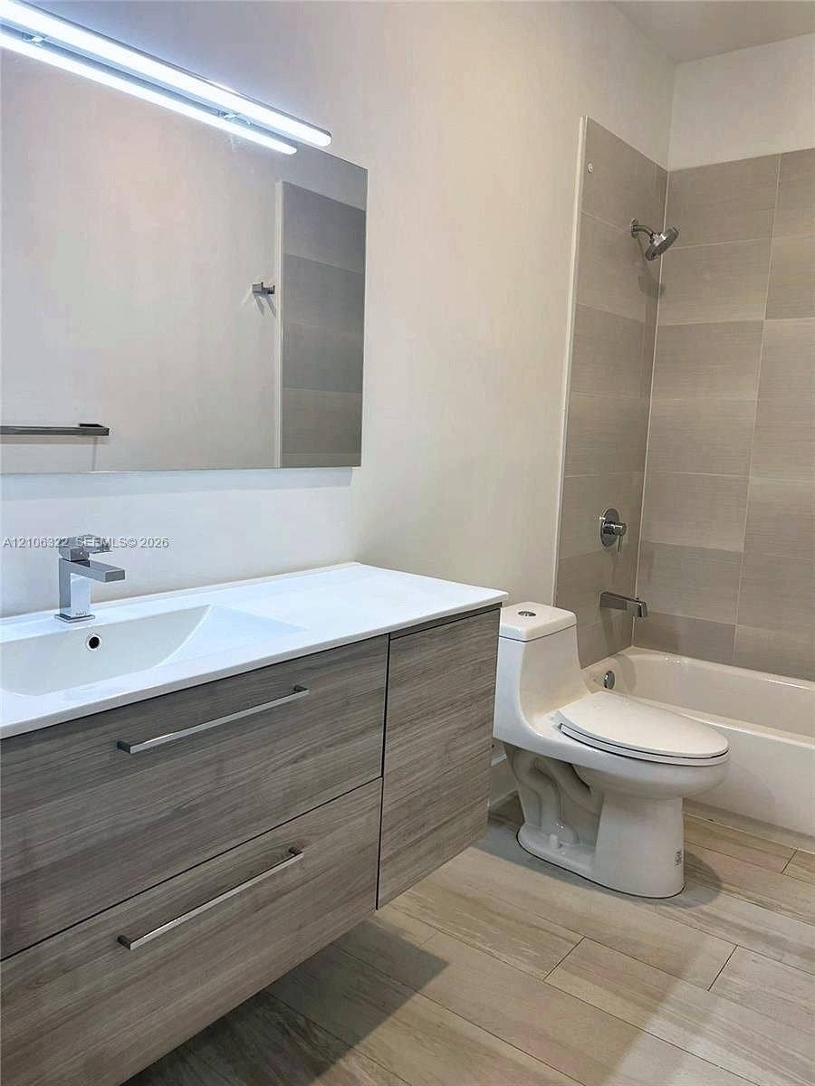 Floating wood-finish vanity with a rectangular sink, large format tile shower surround, and wood-finish flooring