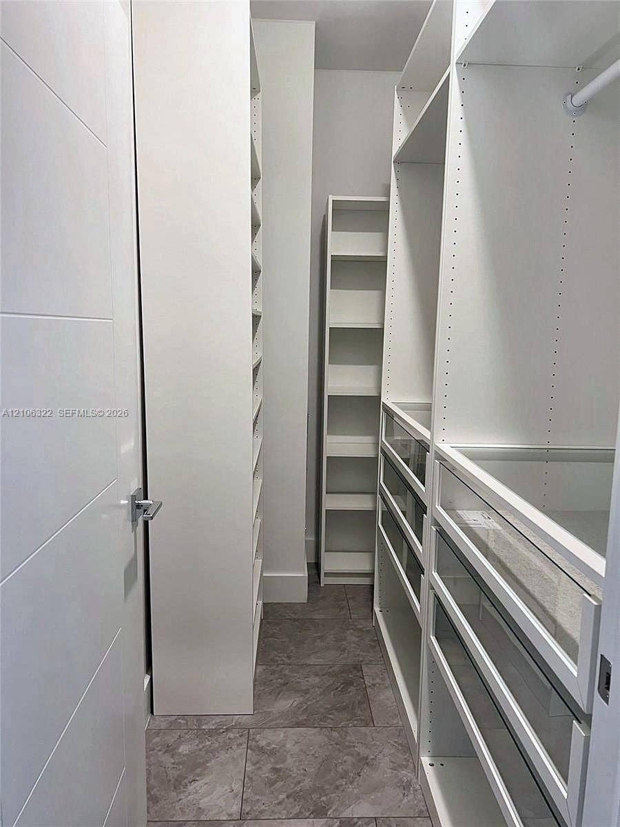 Custom walk-in closet featuring white built-in shelving, glass-front drawers, hanging rods, and stone-finish tile flooring