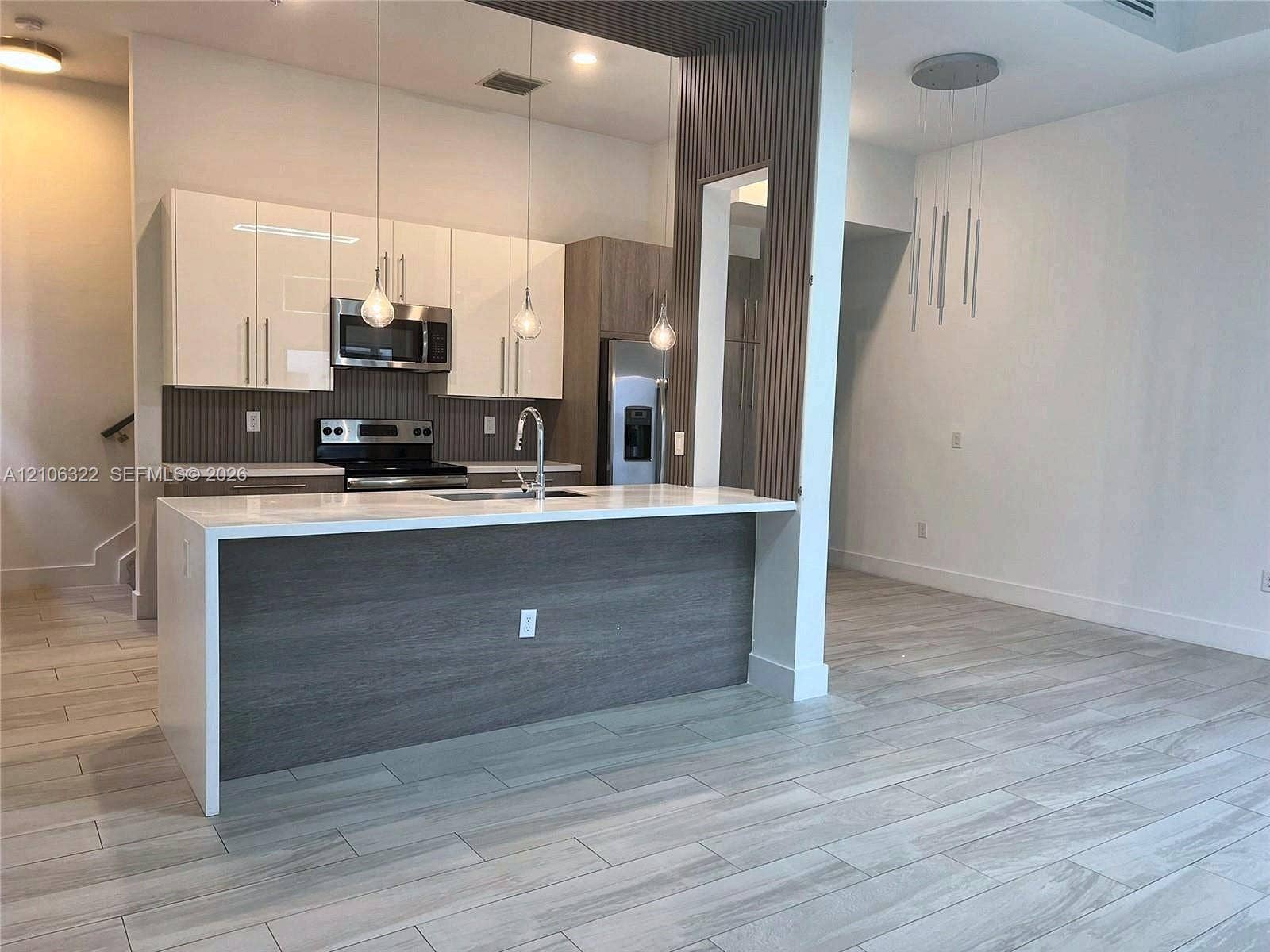 Kitchen featuring high-gloss cabinetry, stone-surface island, wood-finish tile flooring, vertical slat wall detailing, and pendant lighting