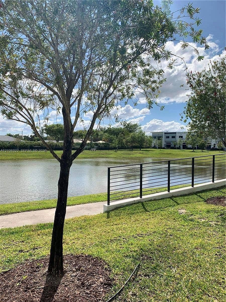 Waterfront lot featuring a concrete walking path, a black metal horizontal railing, and mature trees