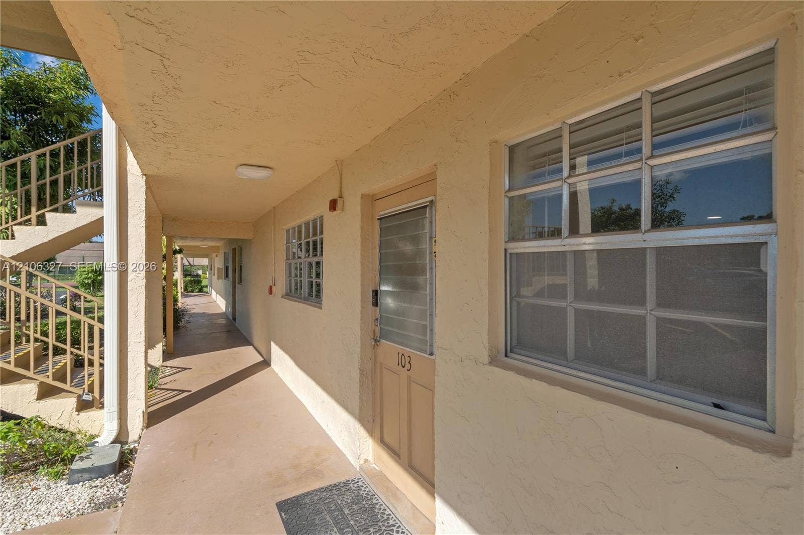 Exterior walkway featuring stucco walls, a metal-framed entry door with integrated glass panel, and metal stair railing