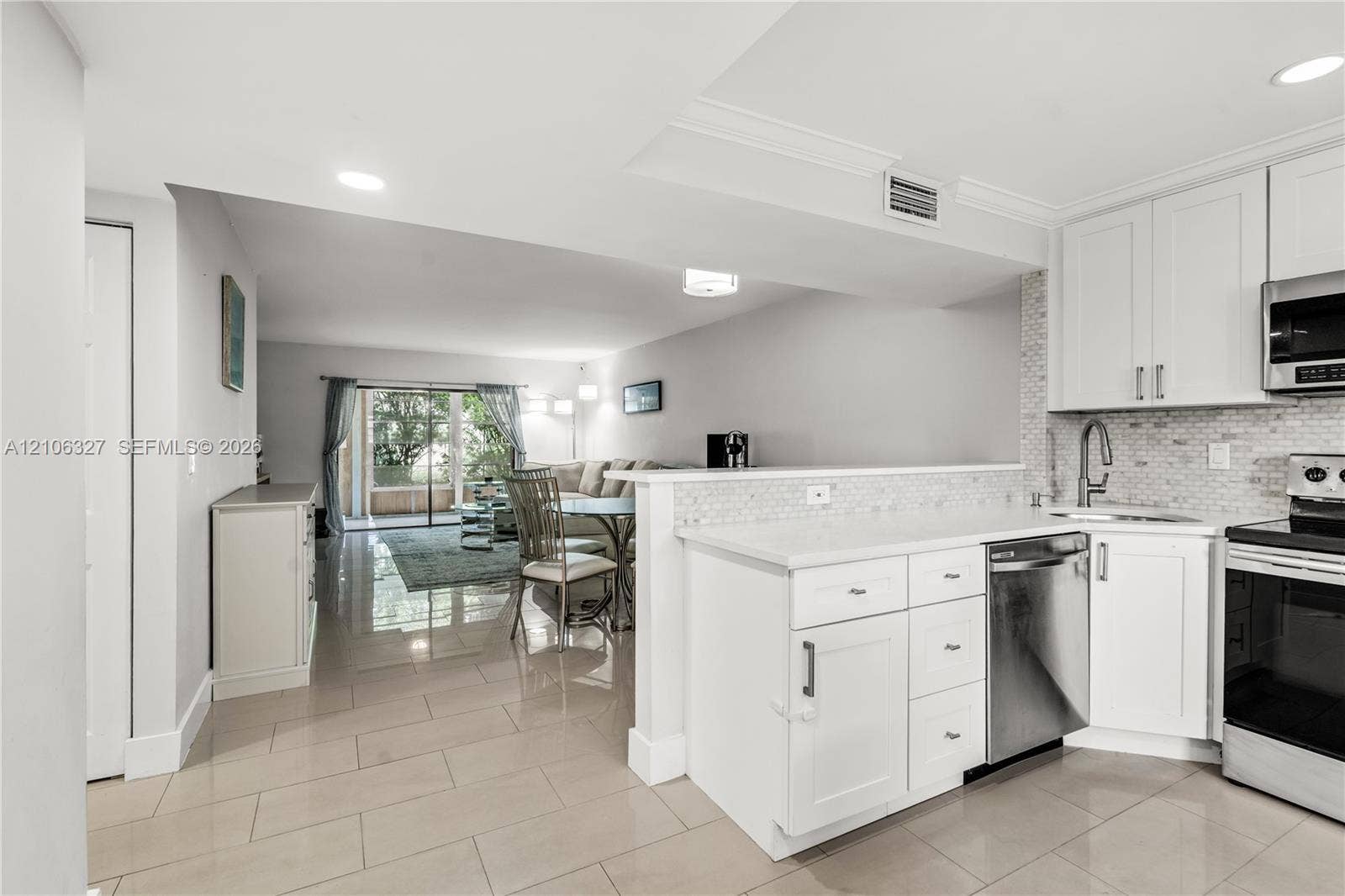Kitchen featuring white shaker-style cabinetry, a mosaic tile backsplash, stainless steel appliances, and large-format tile flooring