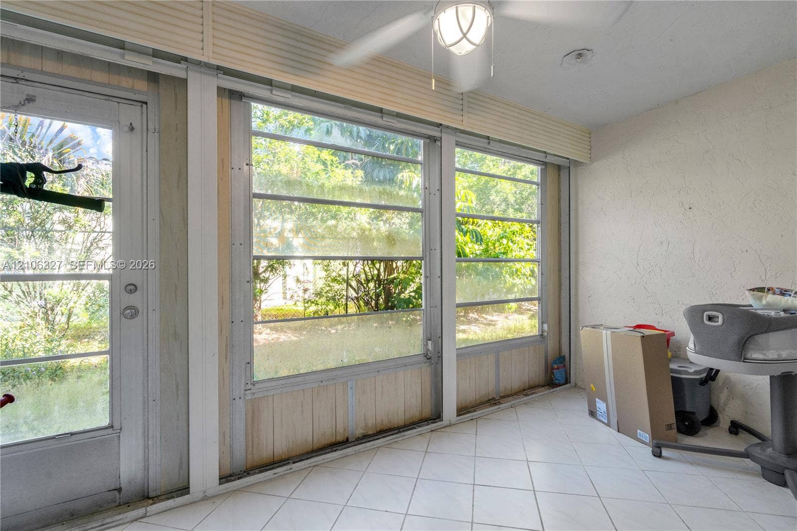Enclosed sunroom featuring white tile flooring, floor-to-ceiling multi-pane windows, a central ceiling fan with an integrated light fixture, and a glass-paneled exterior door