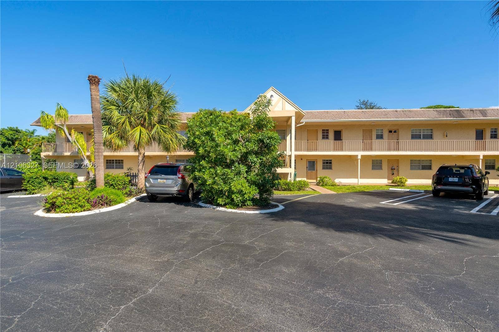 Two-story exterior featuring a gabled roofline, stucco facade, second-level railed balcony, and on-site asphalt parking