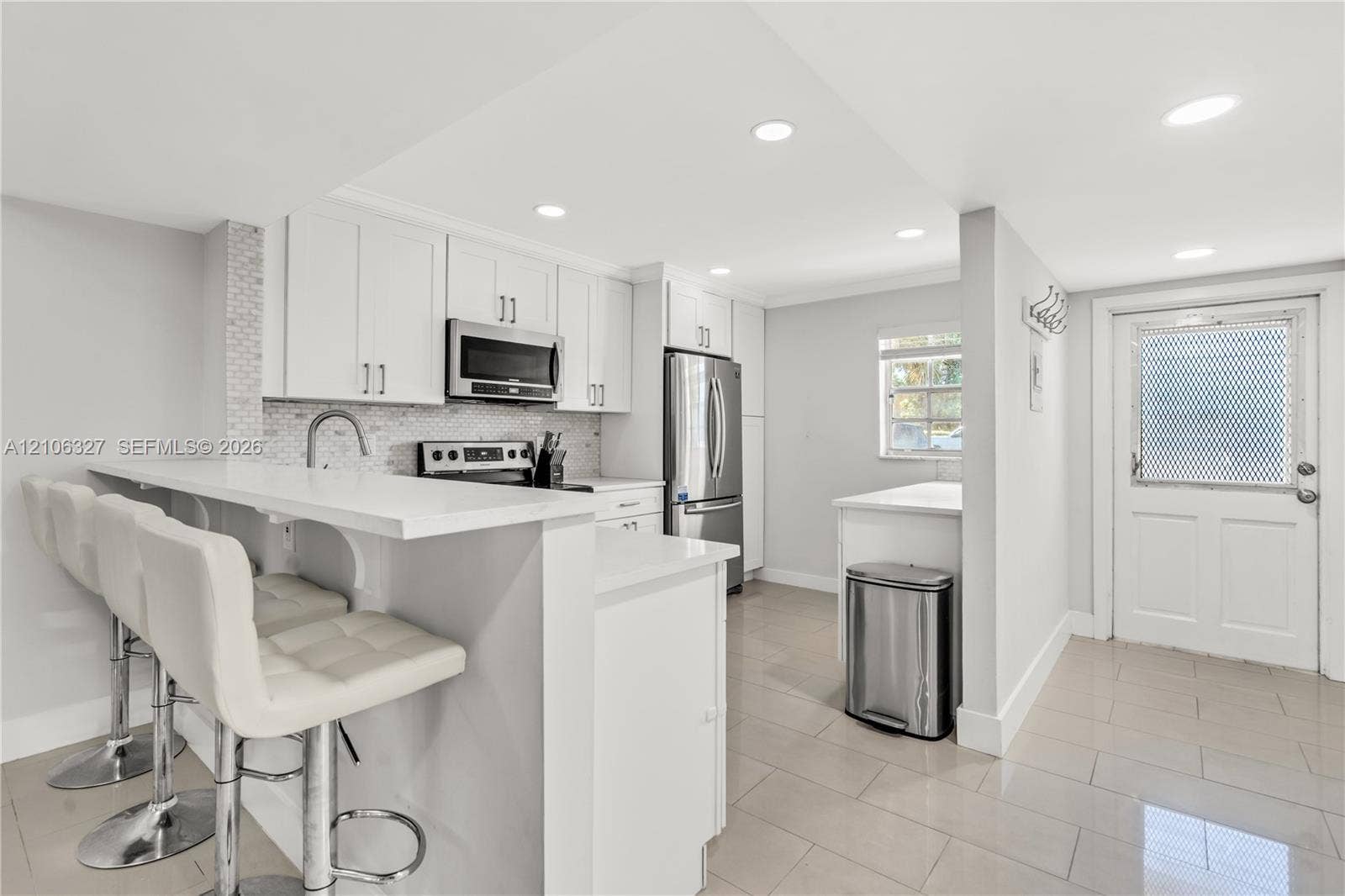 Kitchen featuring white cabinetry, quartz countertops, tile backsplash, stainless steel appliances, and large-format tile flooring