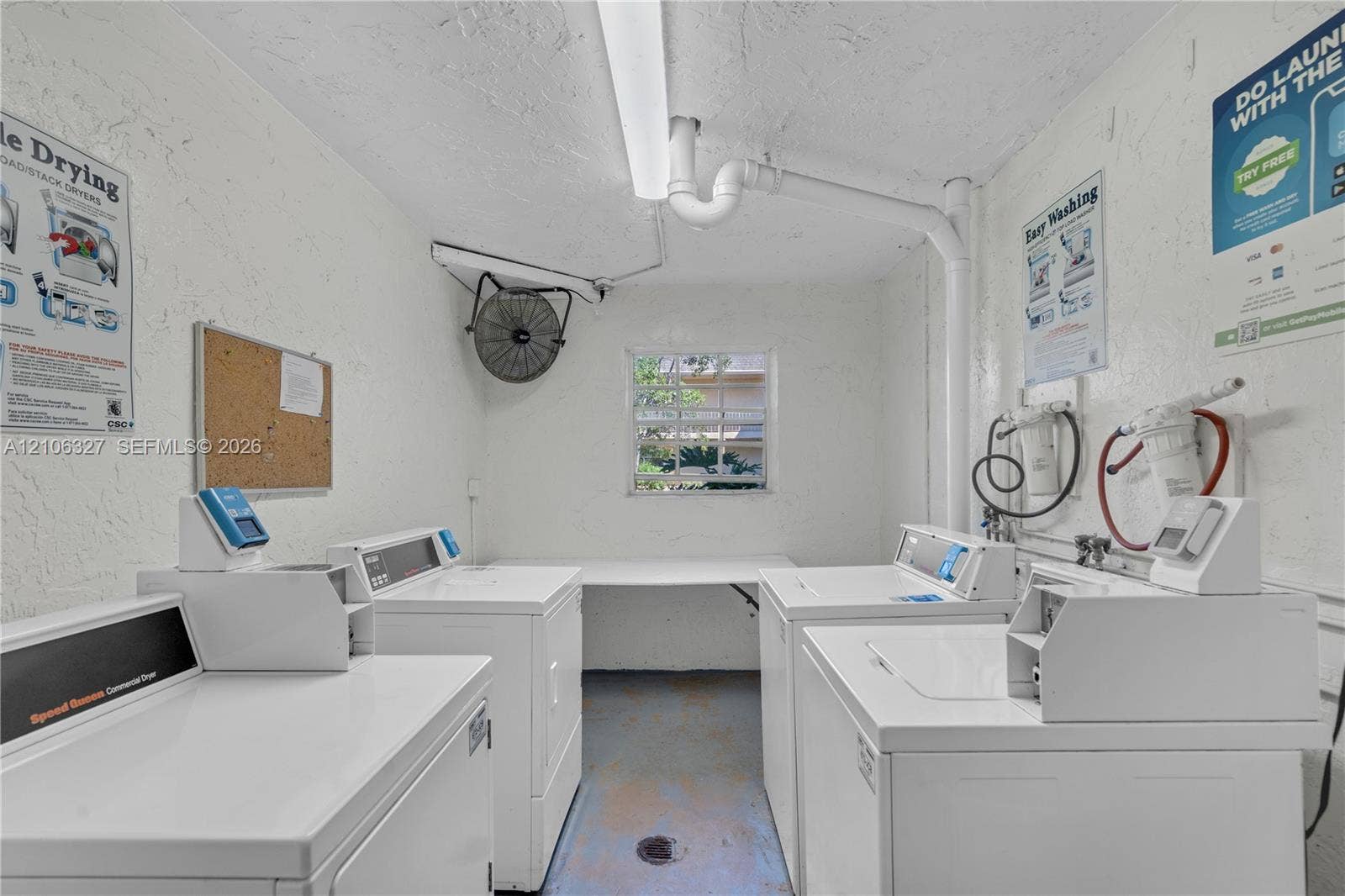 Laundry area featuring commercial-grade washers and dryers, integrated shelving, an exterior-facing window, and wall-mounted exhaust fan