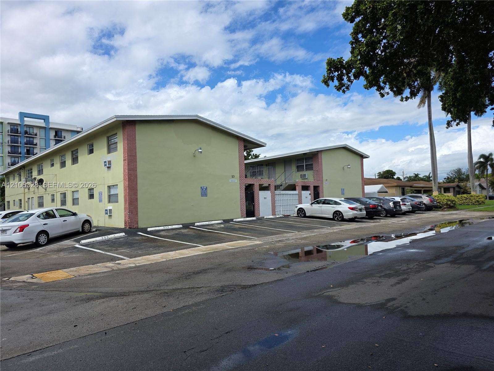Two-story residential building with stucco exterior, brick corner accents, low-pitch roof, and designated surface parking area