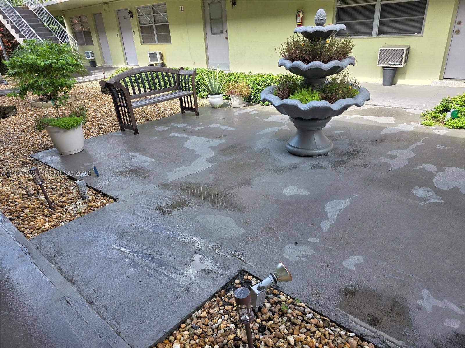 Concrete patio featuring a multi-tiered tiered fountain, gravel landscaping, and metal ground-level accent lighting