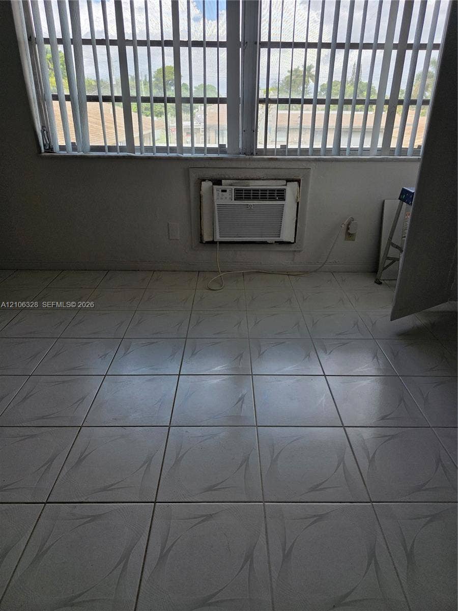 Large-format tile flooring, oversized horizontal window with vertical blinds, and wall-mounted air conditioning unit