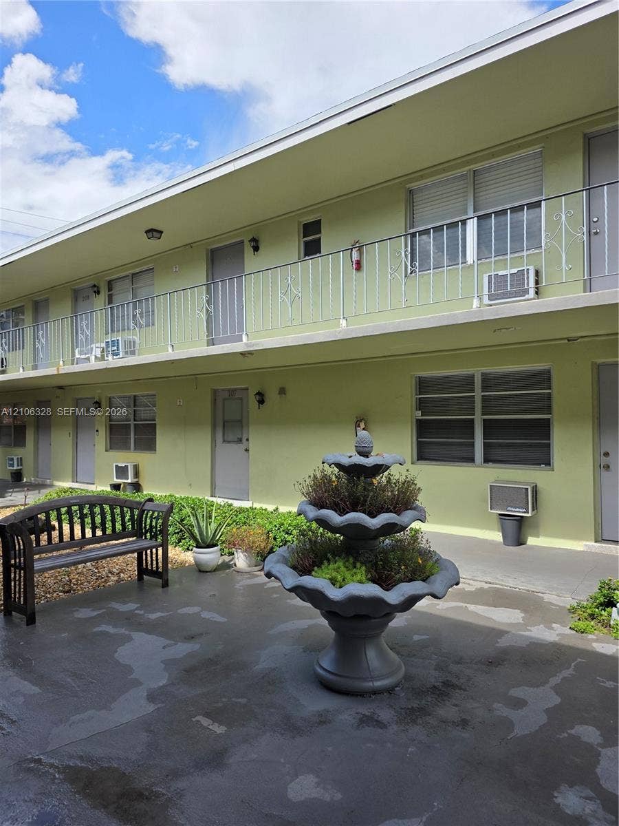 Two-story exterior featuring metal railing, concrete-finish ground level, and decorative multi-tiered stone-finish fountain