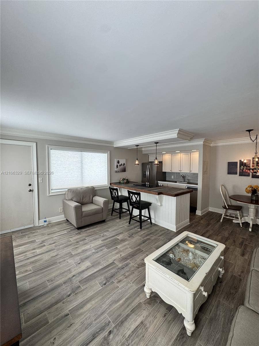 3600 N Ocean Drive, #423, Riviera Beach, Riviera Beach, FL 33404 Wood-finish flooring, kitchen island with wood-tone countertop, white shaker-style cabinetry, crown molding, and pendant lighting