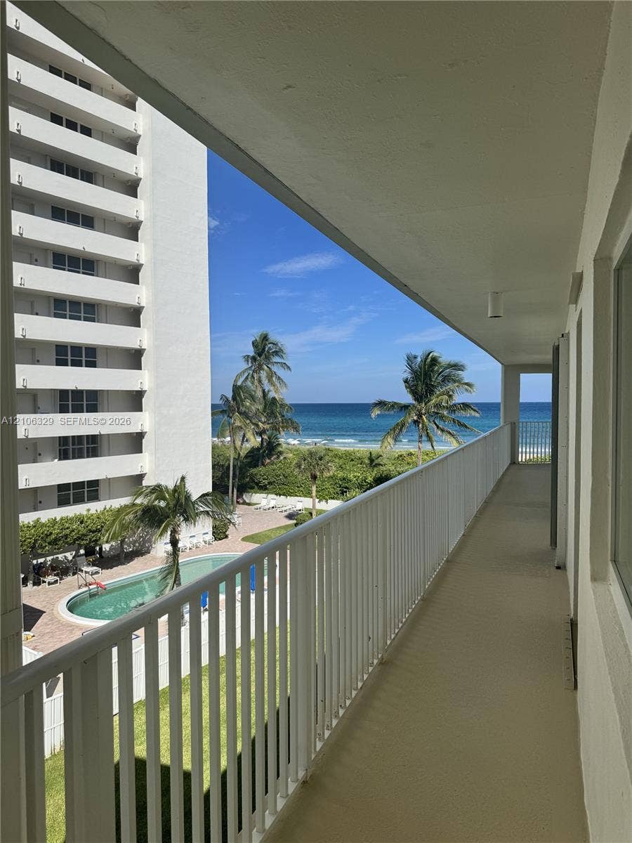 3600 N Ocean Drive, #423, Riviera Beach, Riviera Beach, FL 33404 Covered balcony featuring a white metal railing, concrete flooring, ocean horizon, and direct oversight of the swimming pool and palm landscaping