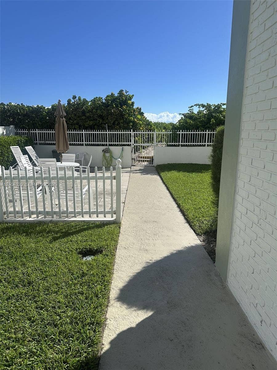 3600 N Ocean Drive, #423, Riviera Beach, Riviera Beach, FL 33404 Backyard featuring a paved patio, white vinyl fencing, a concrete walkway, and a manicured lawn