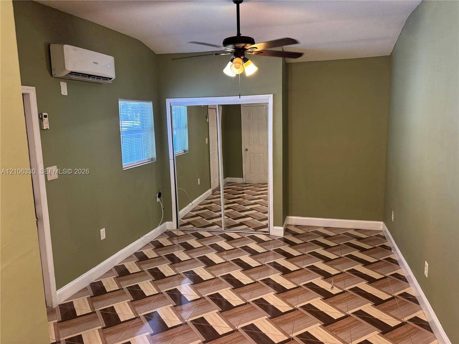 Room featuring patterned ceramic tile flooring, a wall-mounted ductless air conditioning unit, and a ceiling fan with integrated lighting