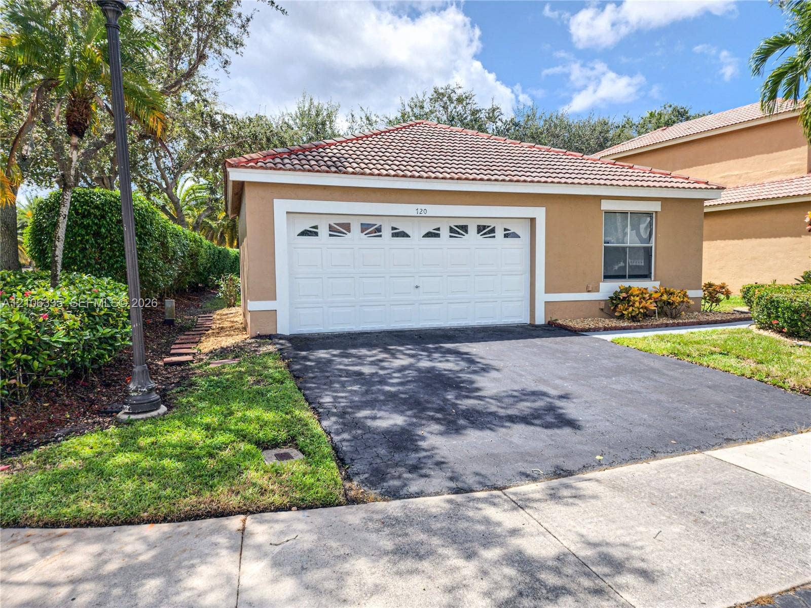 Attached two-car garage featuring a sectional door with arched decorative paneling, stucco exterior, tile roofing, and a paved driveway