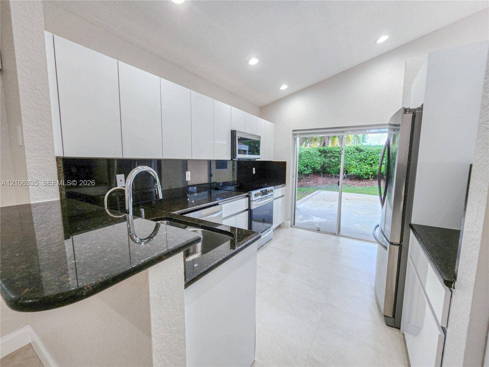 Kitchen featuring white flat-panel cabinetry, dark stone countertops, stainless steel appliances, recessed ceiling lighting, and large-format tile flooring