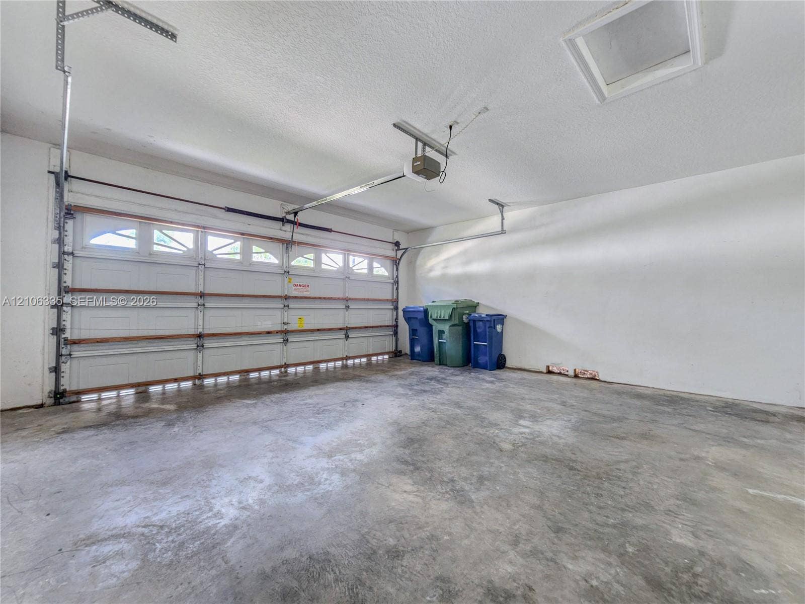 Garage featuring a concrete floor, motorized overhead door with translucent panels, and ceiling access hatch