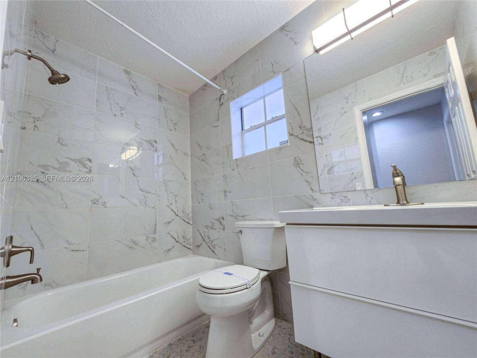 Bathroom featuring floor-to-ceiling veined tile, white vanity with integrated basin, polished metal hardware, and full-width vanity mirror with integrated lighting