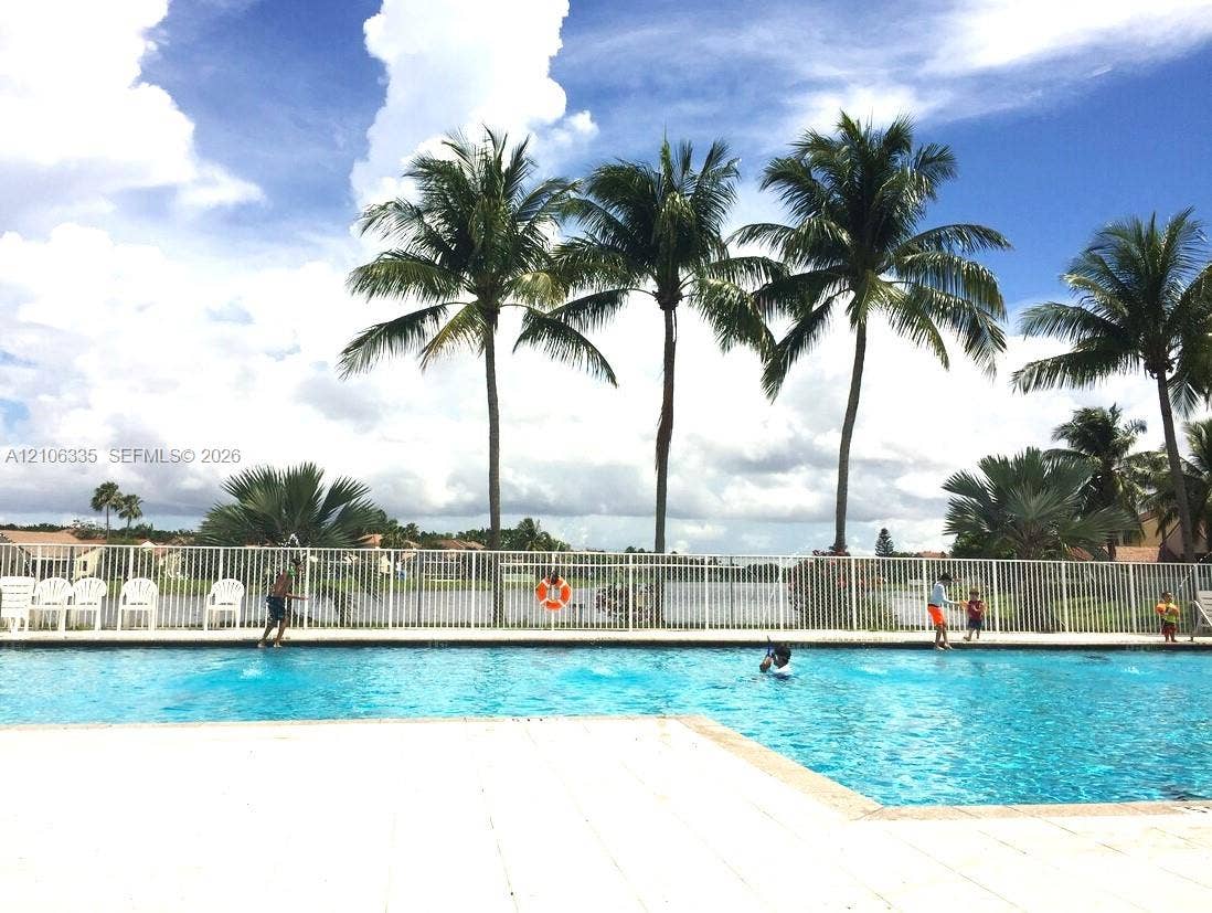 Swimming pool with concrete decking, perimeter metal fencing, and mature palm trees