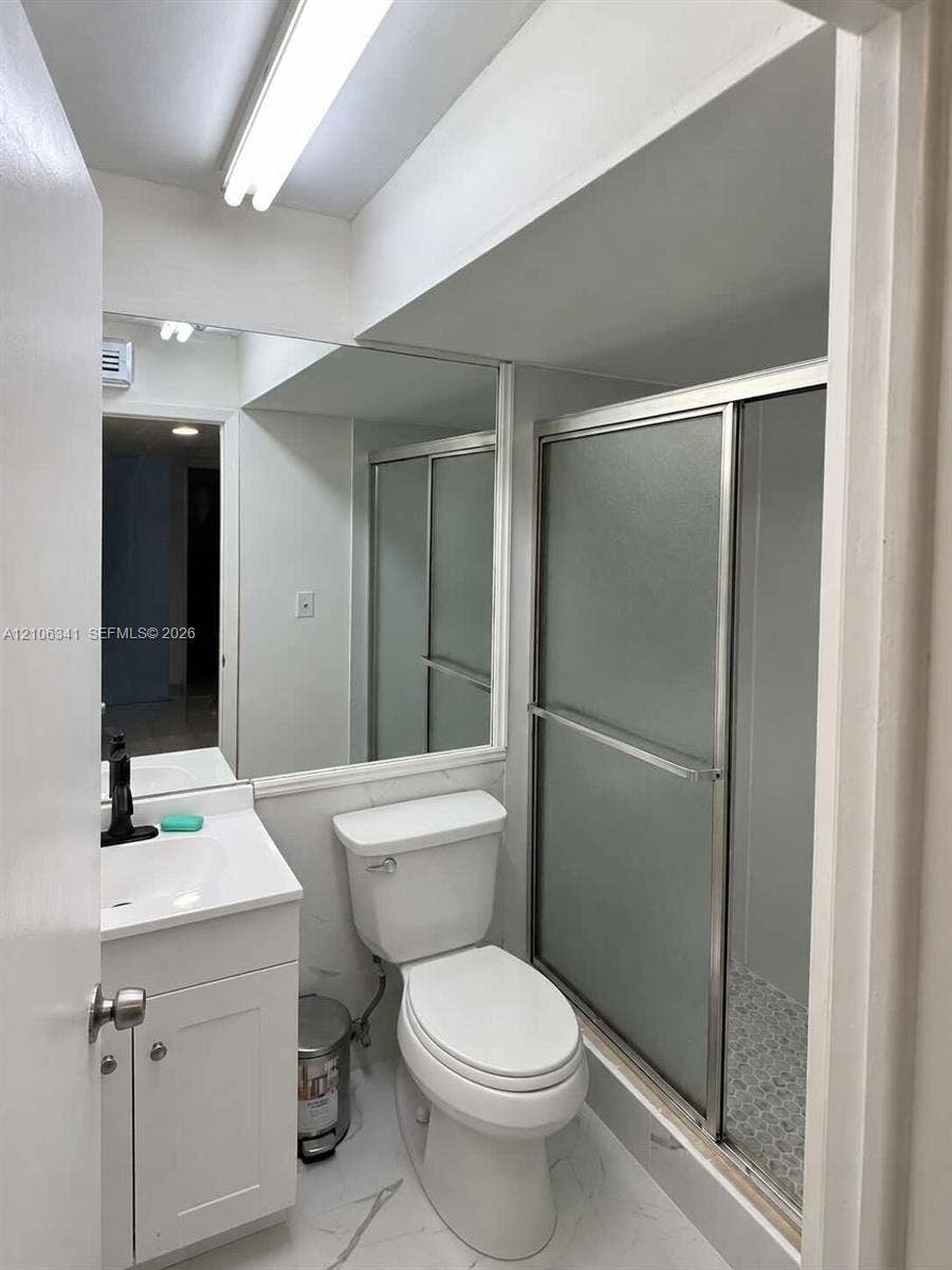 White vanity with a rectangular sink, matte black faucet, wall-spanning mirror, and shower enclosure with frosted glass doors, complemented by stone-pattern tile flooring
