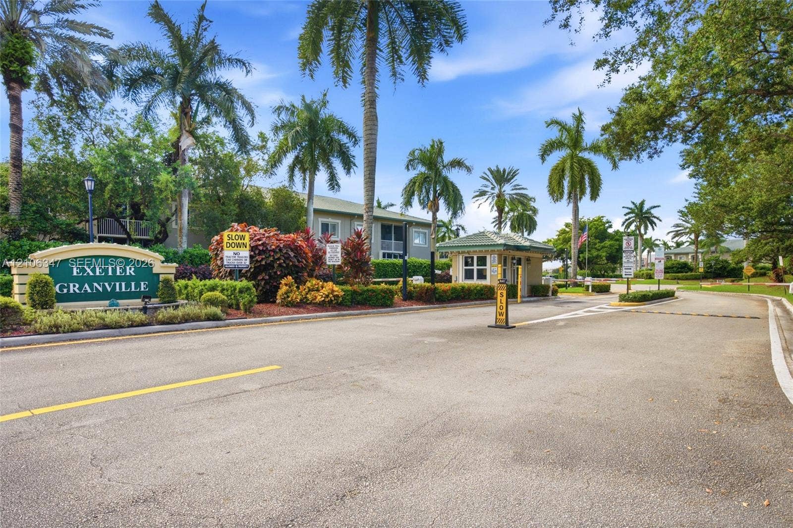 7759 Granville Drive, #306, Tamarac, FL 33321 Gated community entrance featuring a monitored guardhouse, custom signage, mature palm trees, and professional landscaping