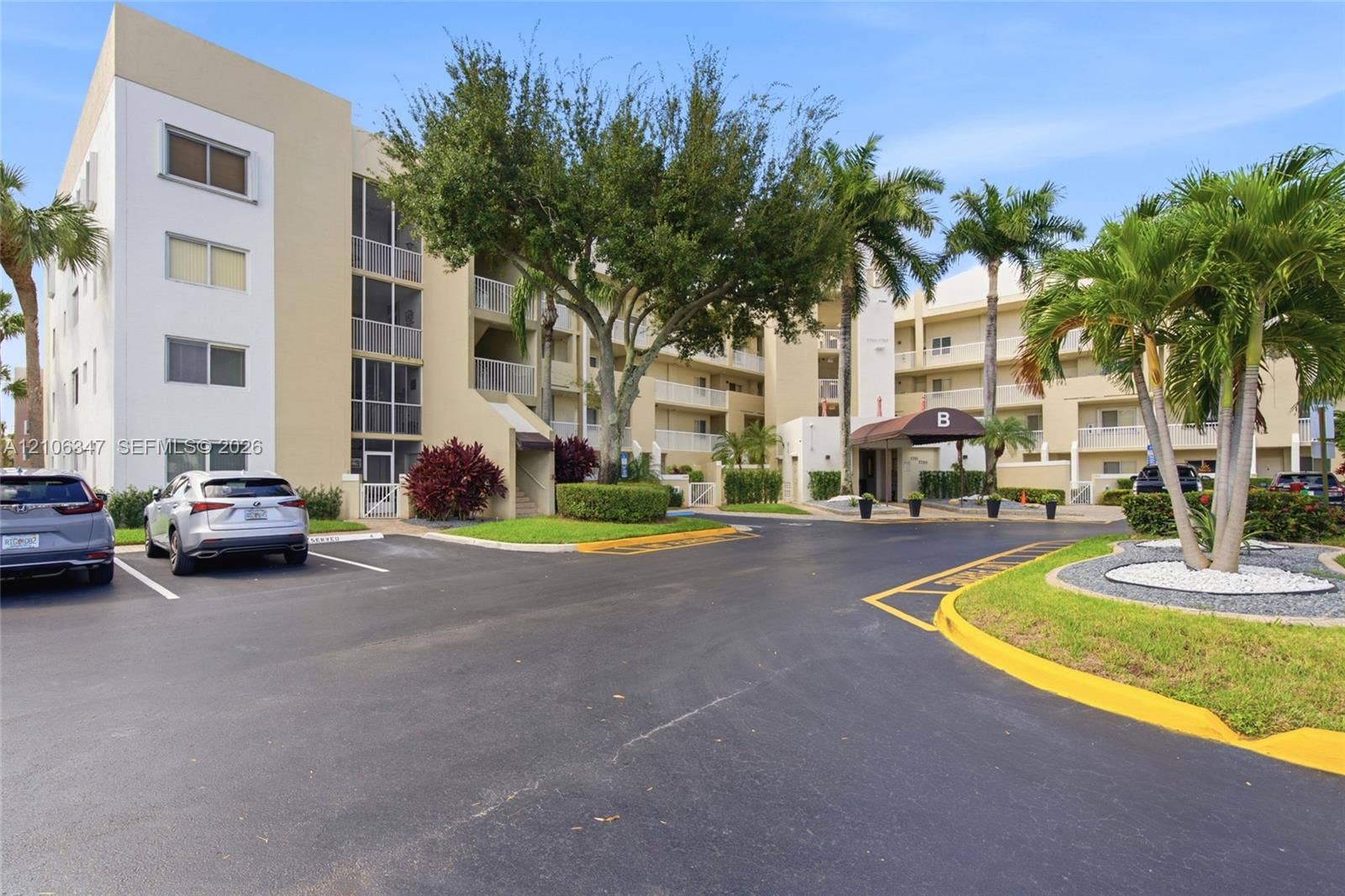 7759 Granville Drive, #306, Tamarac, FL 33321 Multi-story building facade featuring exterior balconies, covered entrance, asphalt parking area, and mature landscaping