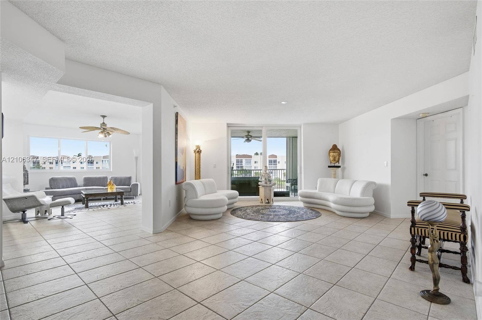 7759 Granville Drive, #306, Tamarac, FL 33321 Open-concept interior featuring large-format neutral floor tile, sliding glass doors providing outdoor access, and a dual-ceiling fan configuration