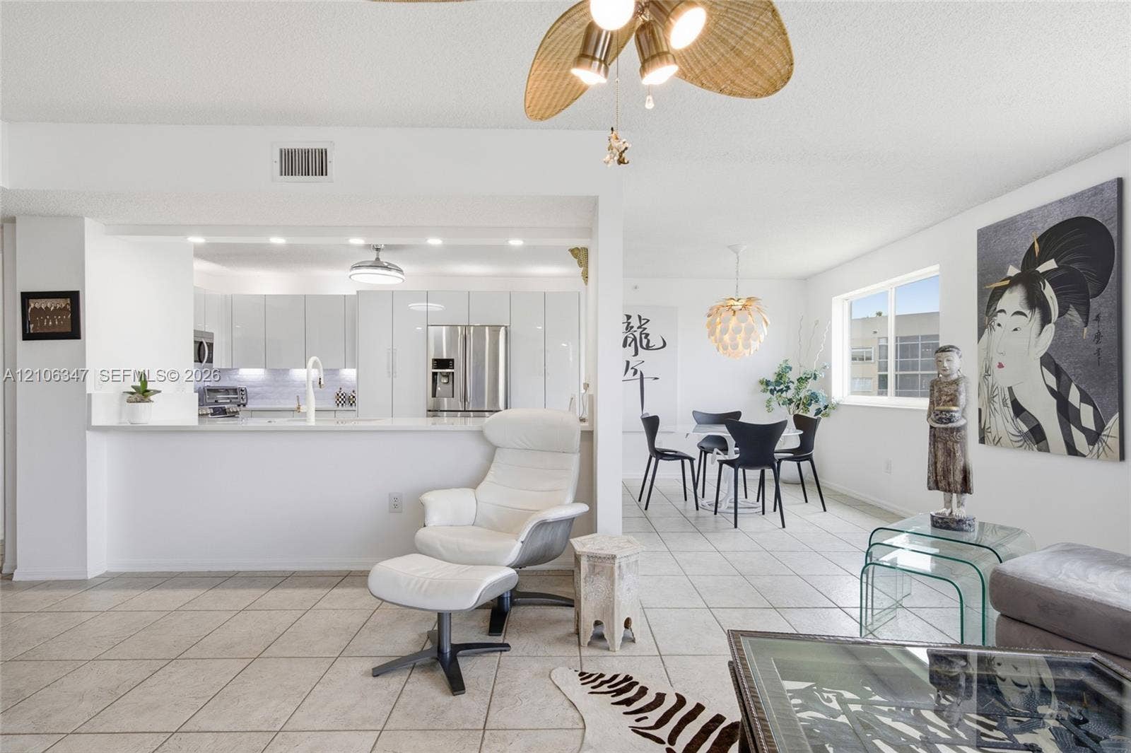 7759 Granville Drive, #306, Tamarac, FL 33321 Open-concept interior featuring light-toned tile flooring, white slab-front cabinetry, stainless steel kitchen appliances, a stone-surface breakfast bar, and decorative ceiling fan with woven-finish blades