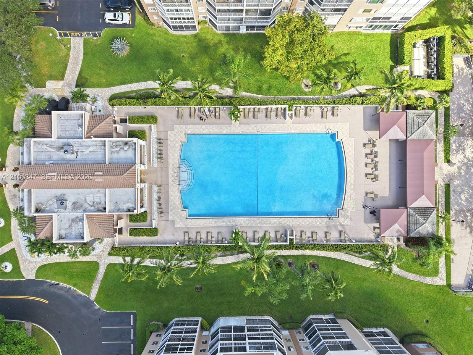 7759 Granville Drive, #306, Tamarac, FL 33321 Aerial perspective of a community pool featuring a paved deck, surrounding mature landscaping, stone-paver walkways, and multiple covered pavilion structures
