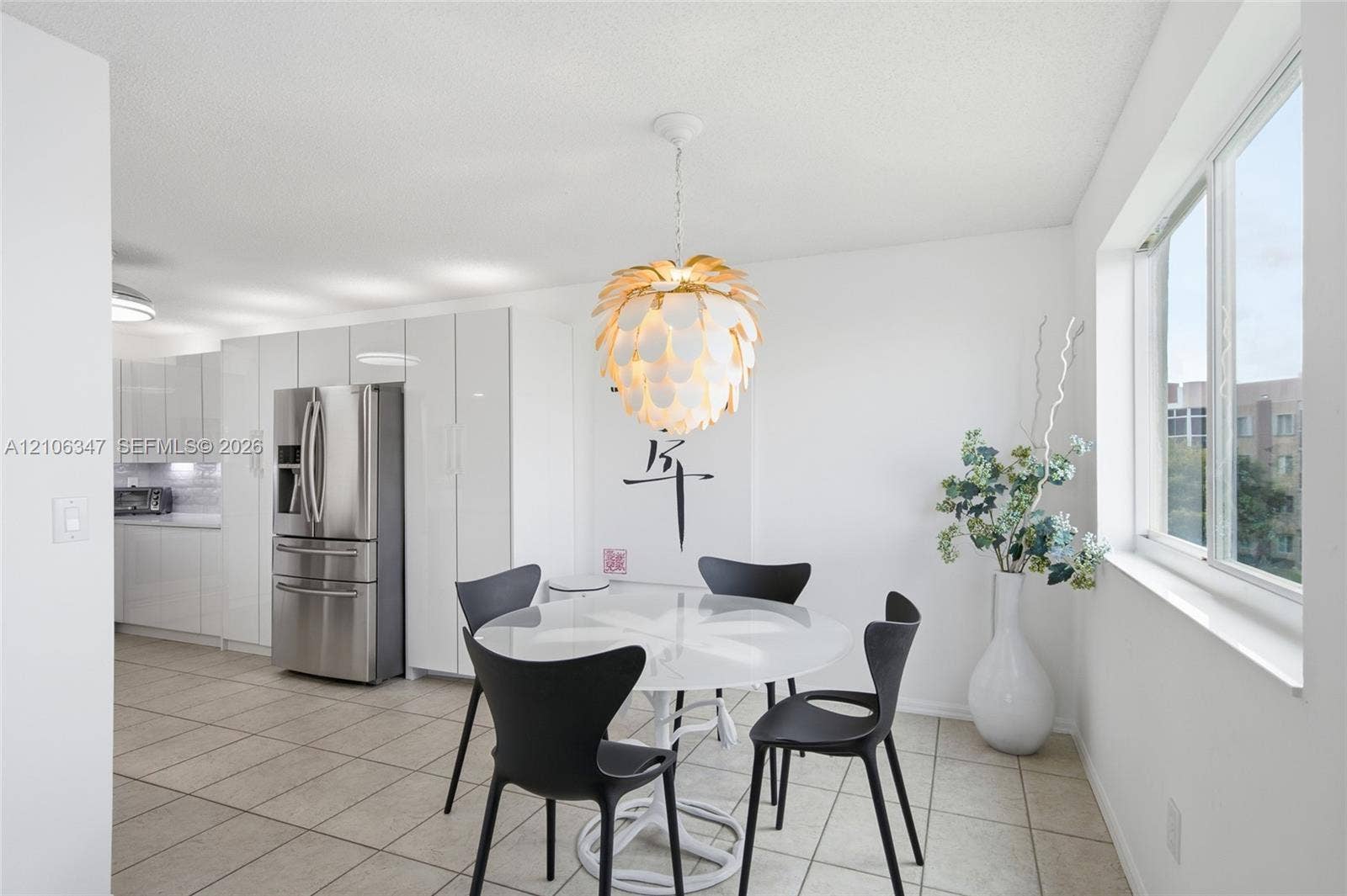 7759 Granville Drive, #306, Tamarac, FL 33321 Modern kitchen featuring high-gloss white cabinetry, stainless steel refrigerator, tile flooring, and a decorative pendant light fixture
