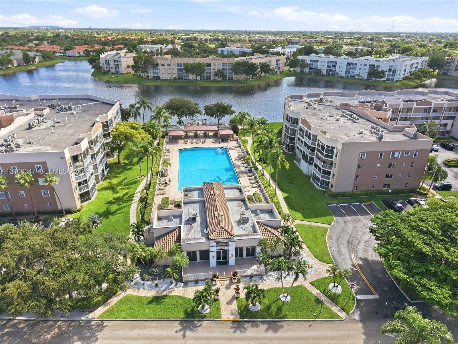 7759 Granville Drive, #306, Tamarac, FL 33321 Community pool area featuring a paved deck, pergola, and direct water frontage with manicured landscaping and mature palm trees