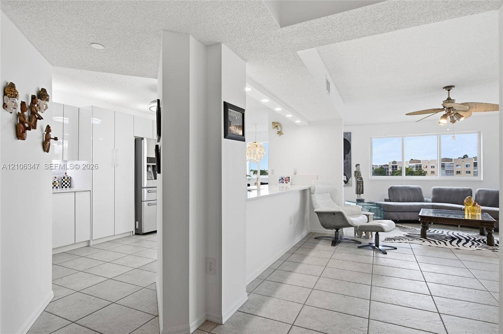 7759 Granville Drive, #306, Tamarac, FL 33321 Kitchen featuring high-gloss white cabinetry, stone-finish countertops, tile flooring, and integrated lighting, including a multi-light ceiling fan